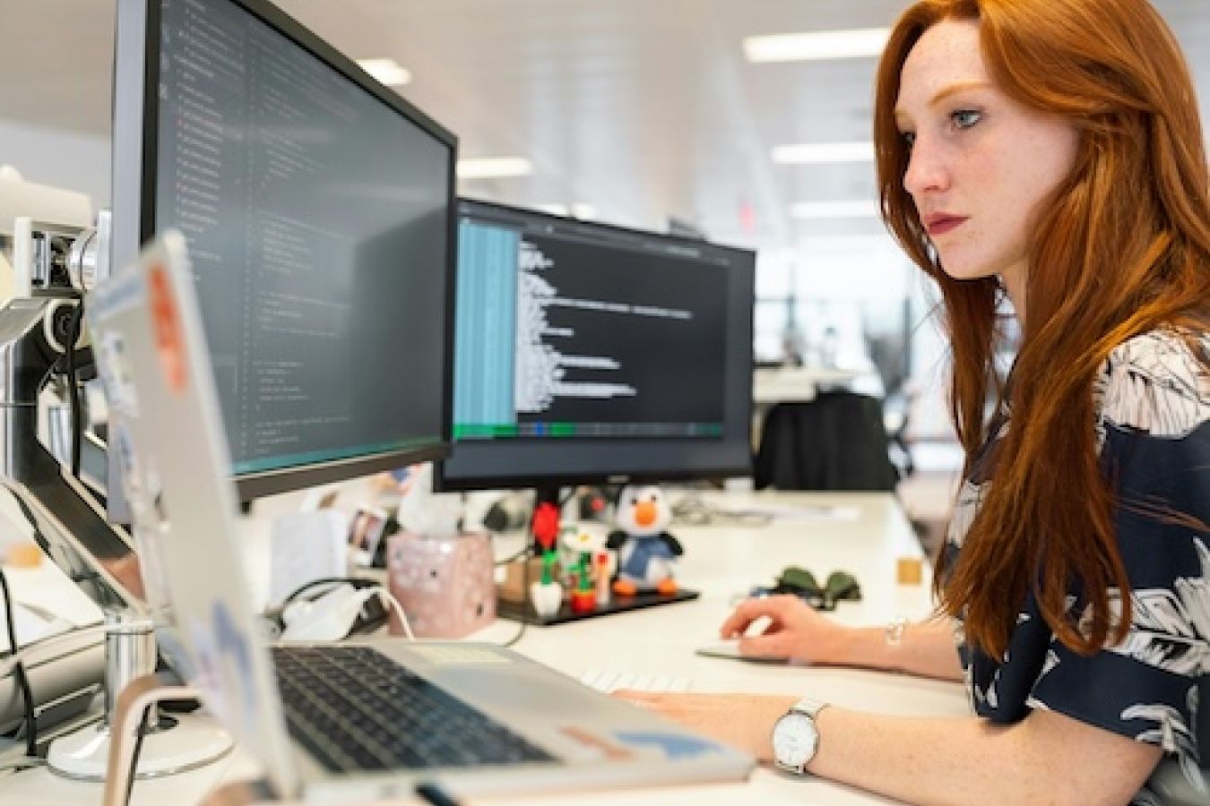 Woman sitting at a printer and looking at code. 