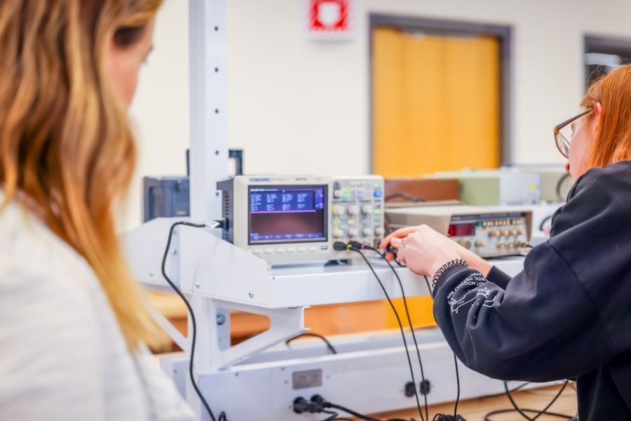 A woman at an electrical switchboard with another person looking on. 