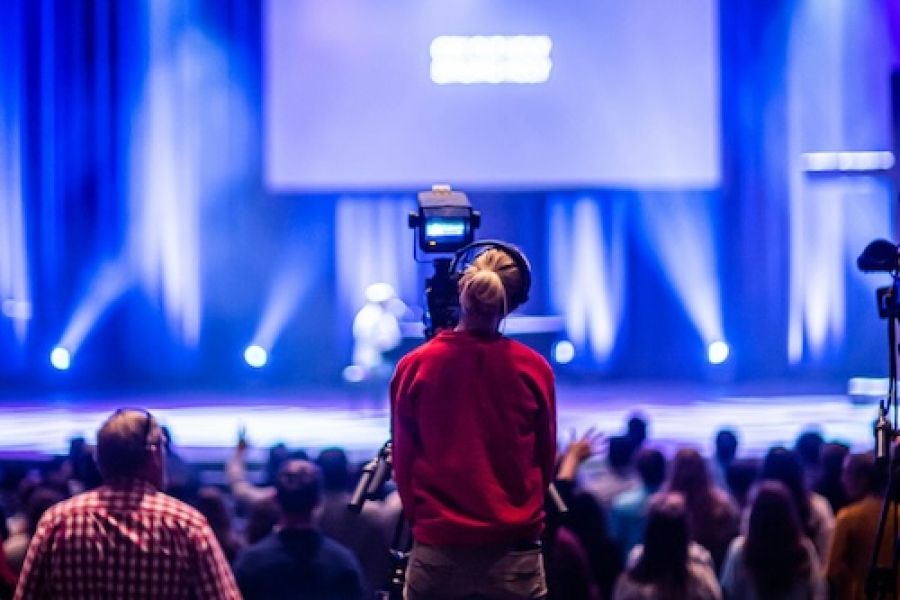 Someone at a camera in front of a huge stage with a crowd. 