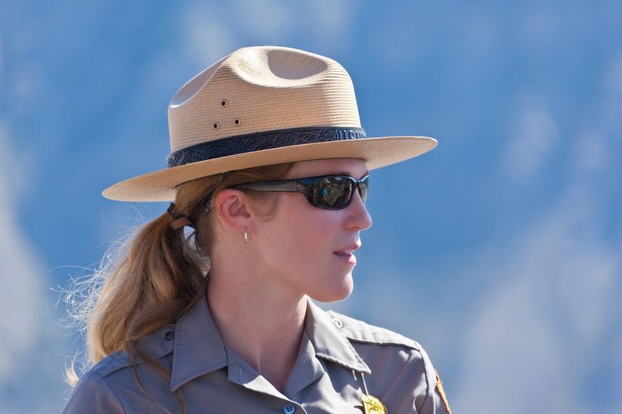 Woman in a park ranger outfit with sunglasses on looking off into the distance. 