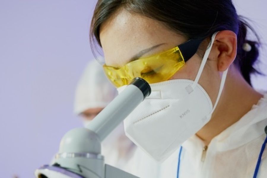 Woman with a mask looking through a microscope 