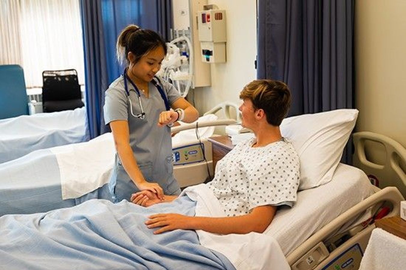 Nursing student takes pulse of patient in hospital bed