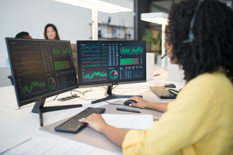 Woman at a computer looking at a bunch of graphs and charts. 