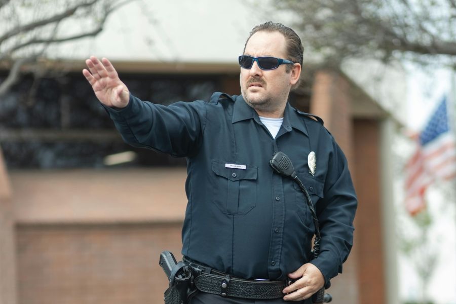 Man in a cop's uniform gesturing for someone to stop. 