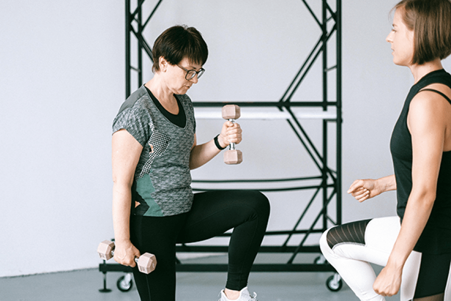 Older woman doing light weights while a woman looking on, coaching her. 